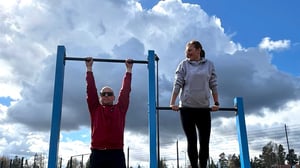 Homme et femme pratiquant un entraînement en plein air sur une barre de traction dans une aire de street workout avec barre de traction extérieure Omnigym.