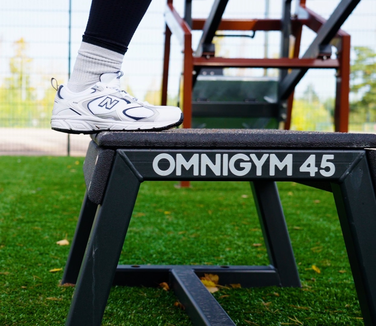 Feet standing on a 45 cm high plyo box with the Omnigym logo, in an outdoor gym.