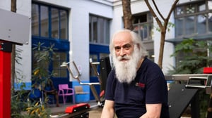 Senior man taking a break between repetitions while exercising on Omnigym outdoor gym equipment at an Emmaüs Solidarité shelter for people experiencing homelessness in Paris, France, highlighting accessible outdoor fitness facilities in a community support environment.