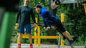 Two men smiling while performing a Adjusted Back Extension exercise at an Omnigym outdoor gym.