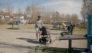 pappa med barnvagn tränar på ett utegym en solig vårdag