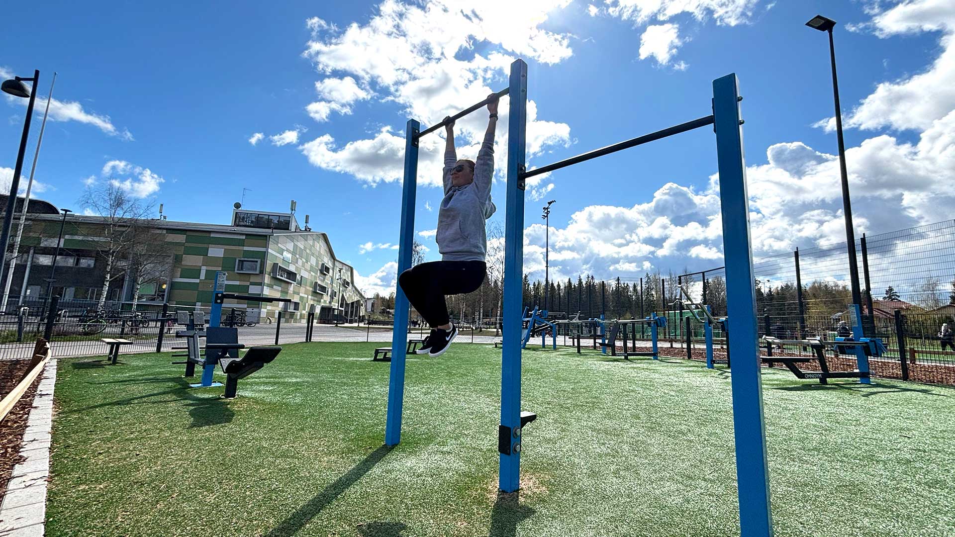 Femme réalisant des relevés de genoux sur une barre de traction dans une aire de street workout avec barre de traction extérieure Omnigym, en plein air dans un espace de fitness extérieur. Femme réalisant des relevés de genoux sur une barre de traction dans une aire de street workout avec barre de traction extérieure Omnigym, en plein air dans un espace de fitness extérieur.